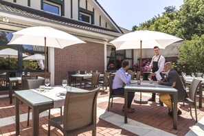 Un área de comedor al aire libre con mesas, sillas, sombrillas y un muro de ladrillo.
