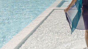 Zona junto a la piscina con borde de agua transparente y un paseo enlosetado.
