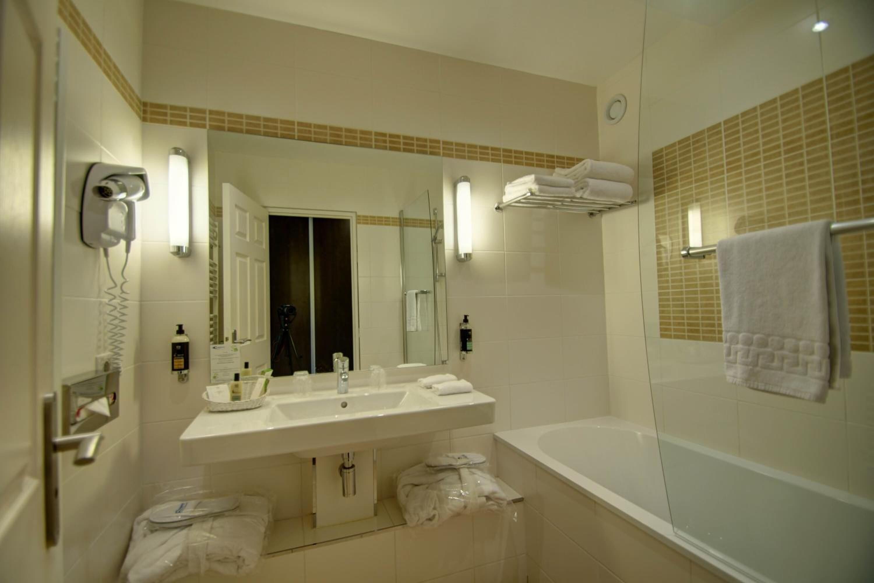 Ein Badezimmer mit Waschbecken, Spiegel und Dusche. Handtücher und Pflegeprodukte sind sichtbar.