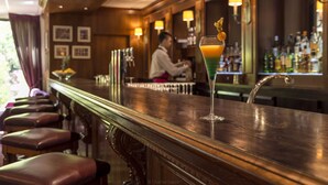 Un bar con una barra de madera pulida, un cantinero al fondo y un cóctel sobre la barra.