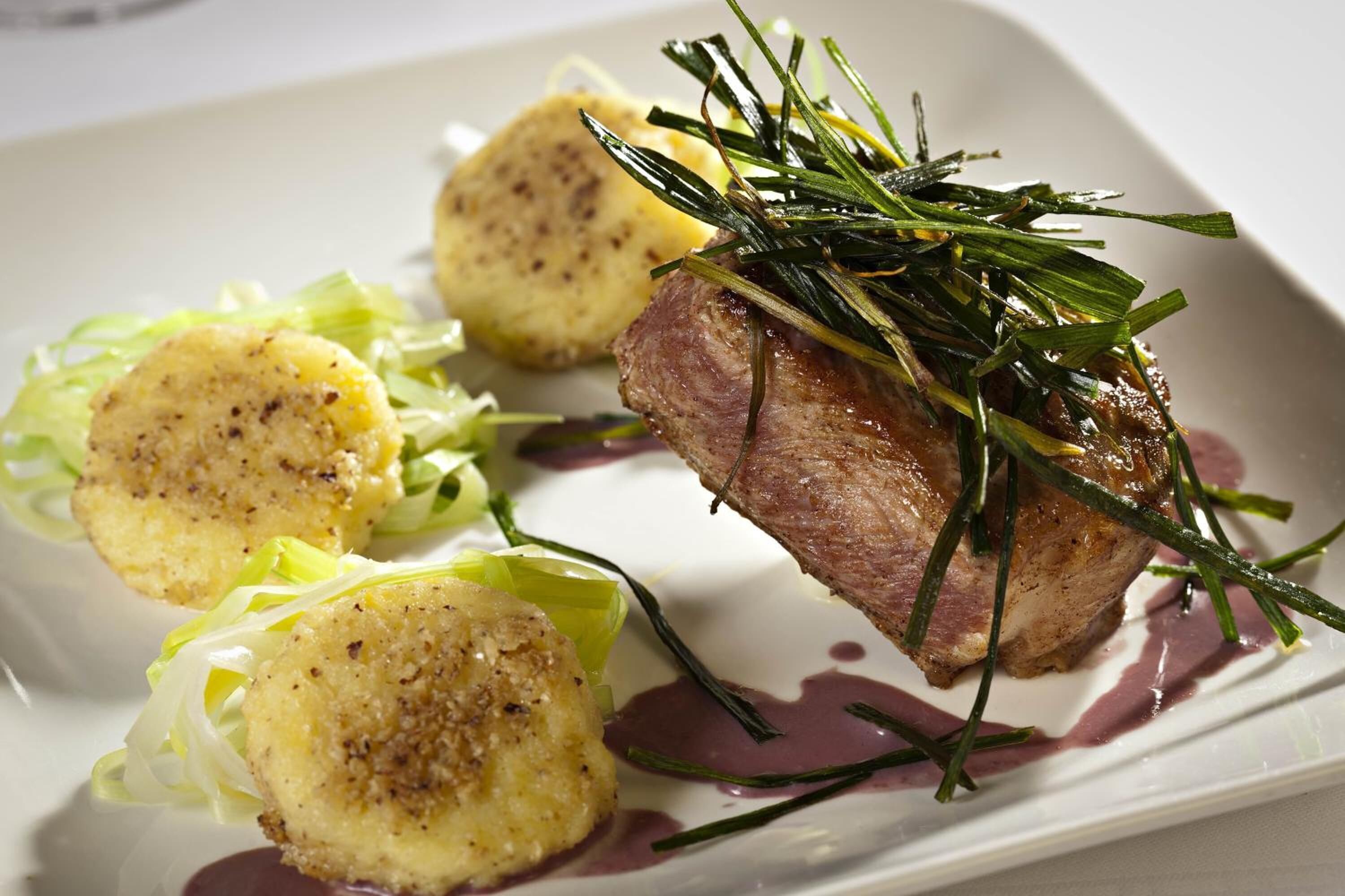 A plated dish with a piece of meat, potato dumplings, and a side of greens.