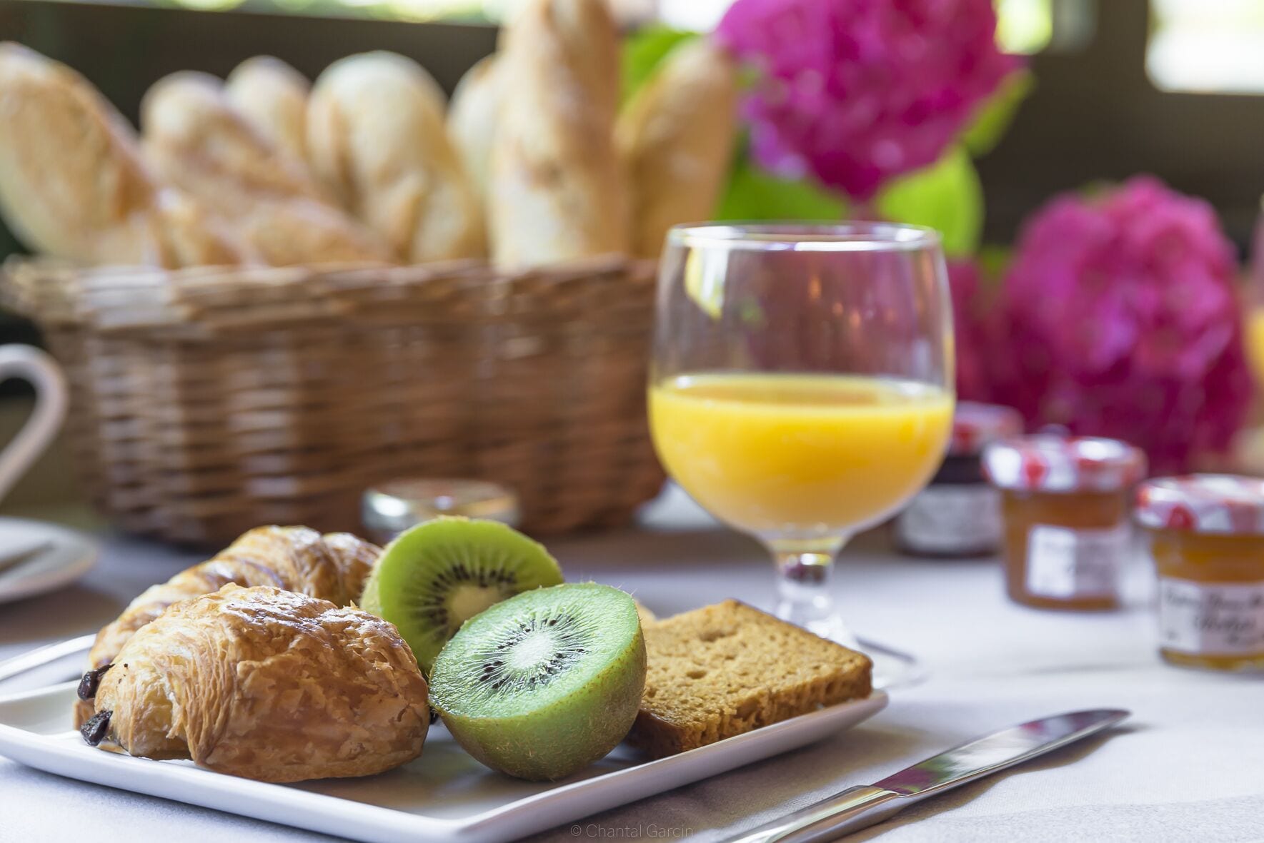 Una mesa con pasteles, kiwi en rodajas, tostadas y un vaso de zumo de naranja.