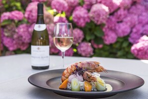 Un plato de mariscos con arroz y vegetales, una copa de vino blanco y una botella de vino sobre una mesa con un fondo floral.