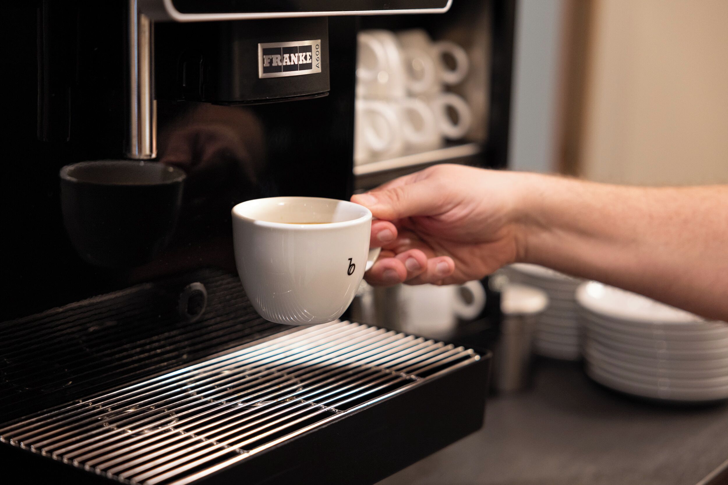 Una mano sosteniendo una taza blanca cerca de una máquina de café con una etiqueta que dice 'FRANKE'.