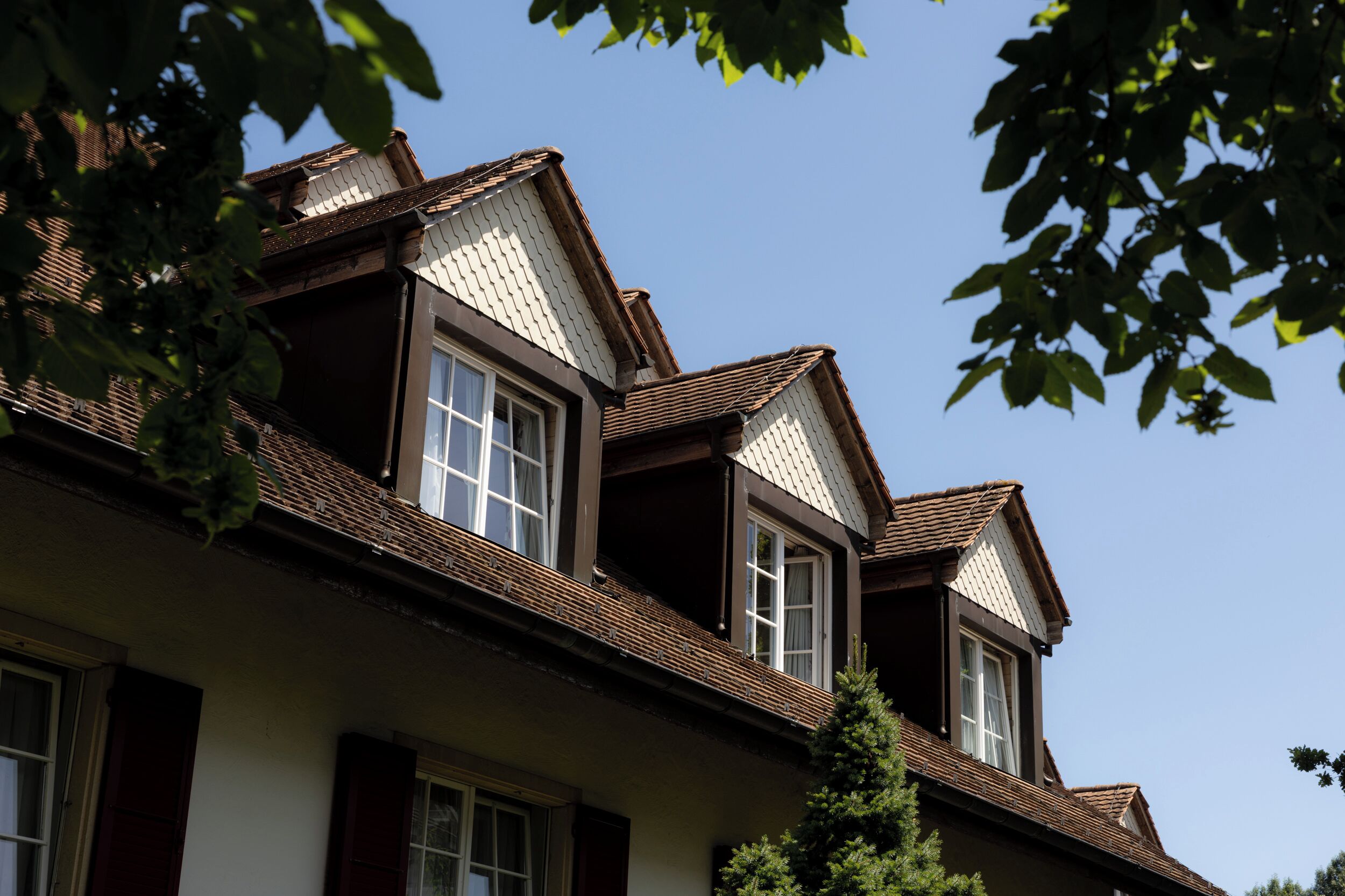 Una casa de dos pisos con techo inclinado, ventanas de dormer y una chimenea visible.