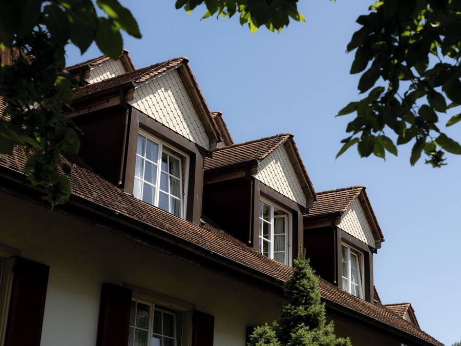 Uma casa de dois andares com telhado íngreme, janelas de sótão e chaminé aparente.