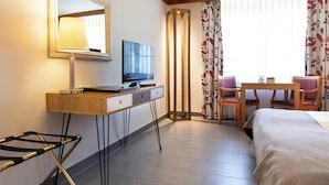 Habitación de hotel con cama, escritorio con televisor, lámpara, silla y mesa.