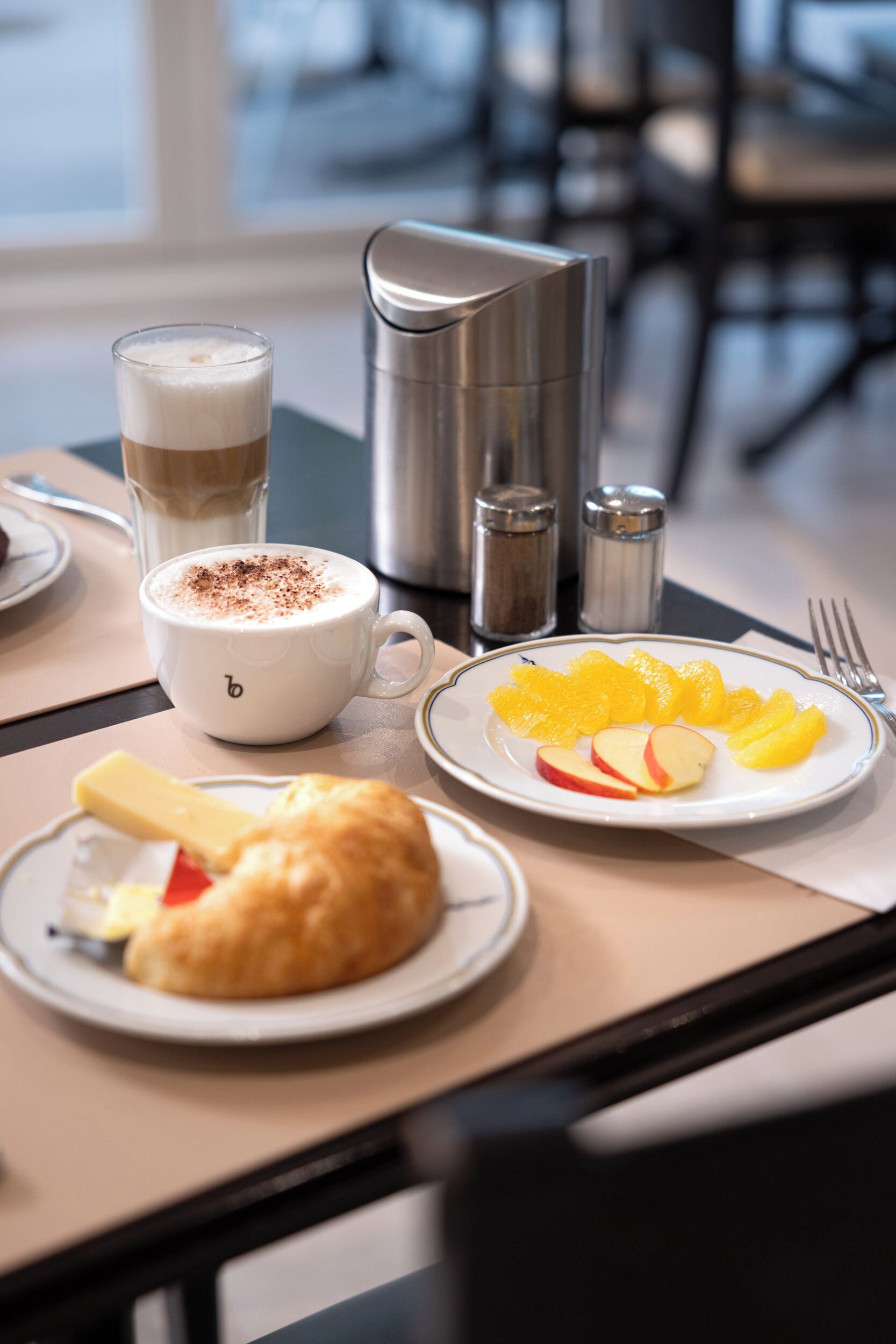 Une table mise pour le petit-déjeuner, avec une tasse de café, une assiette de fruits et une pâtisserie.