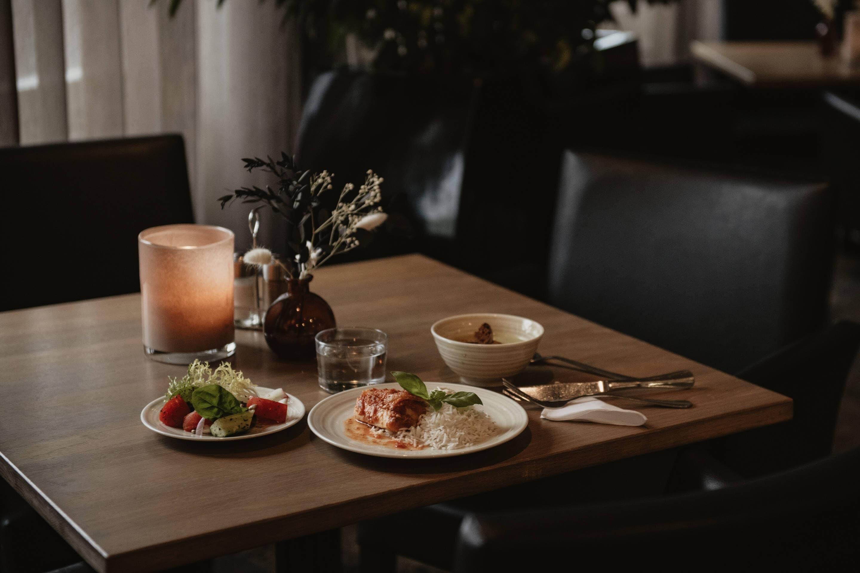 Une table à manger avec une assiette de nourriture, une bougie et un vase contenant des fleurs séchées.