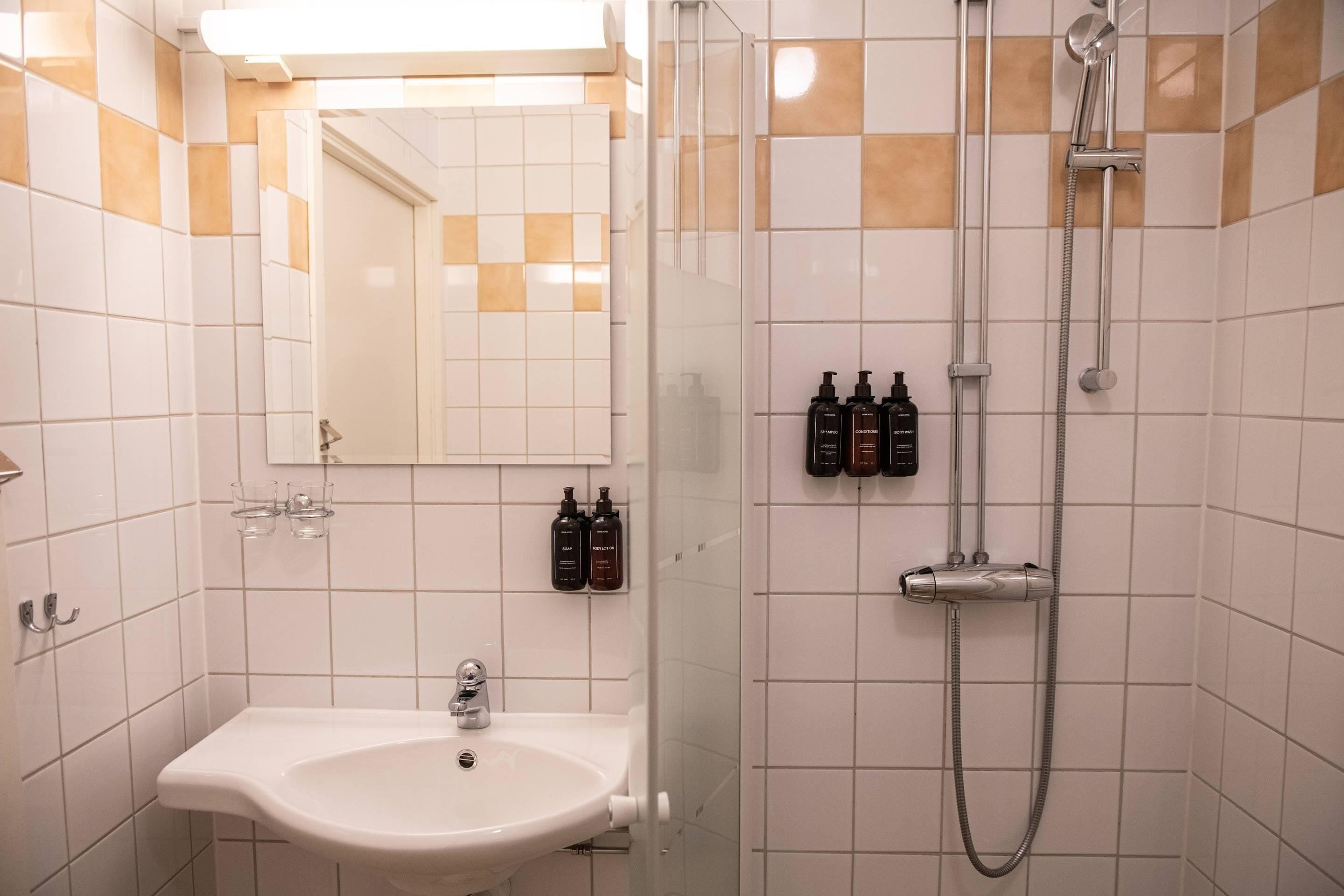 Un baño con lavamanos, espejo, ducha y artículos de aseo.