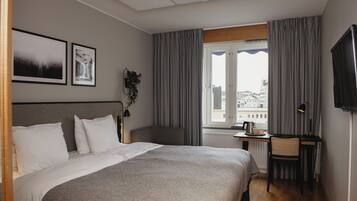 A hotel room with a bed, a desk, a chair, a TV, and a window with curtains.
