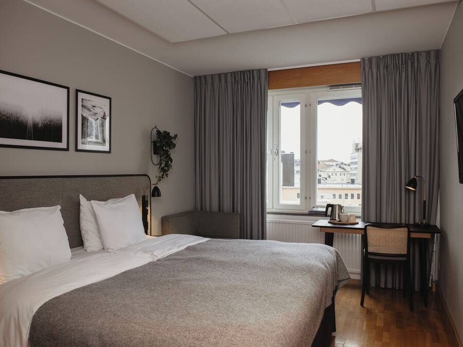 A hotel room with a bed, a desk, a chair, a TV, and a window with curtains.