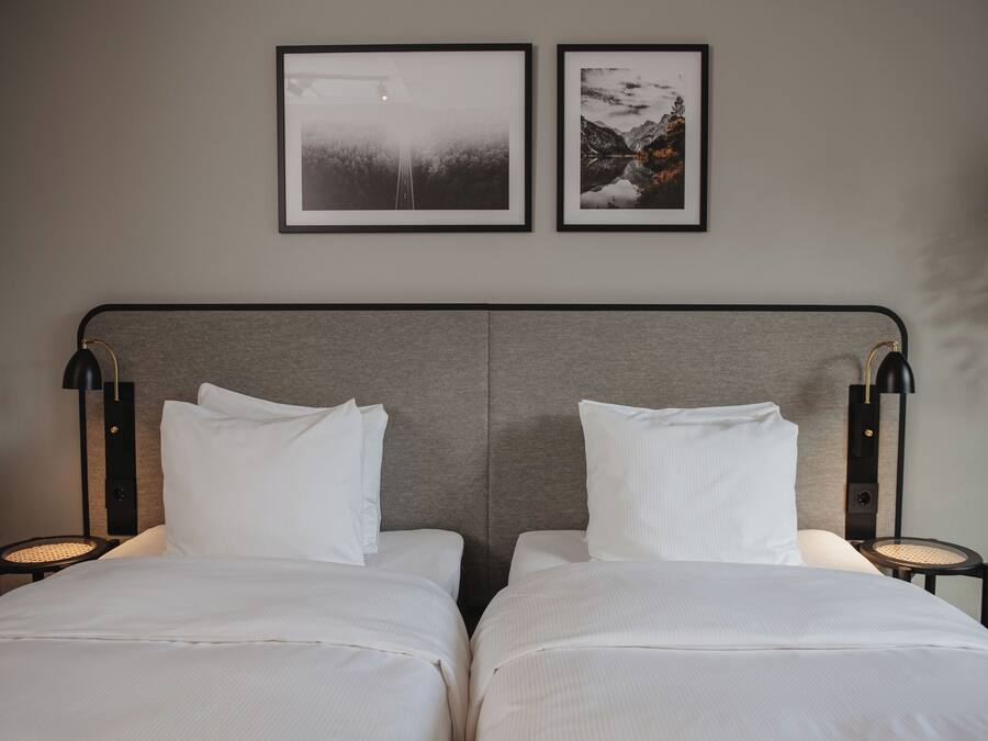 A double bed with a grey headboard, two bedside tables with lamps, and two framed pictures on the wall.