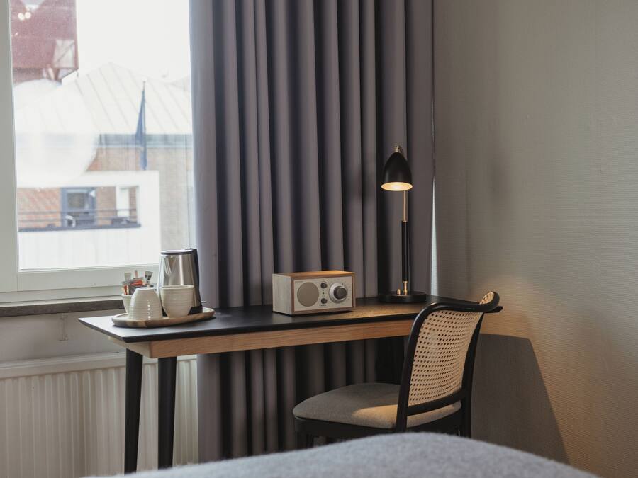 Habitación de hotel con escritorio de madera, una silla, un radio y una lámpara.
