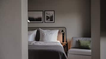 A bedroom with a bed, a nightstand, a lamp, a sofa, and two framed pictures on the wall.
