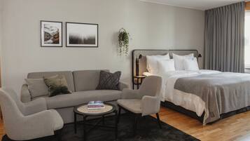 A modern bedroom with a grey sofa, a small round table, a bed with white bedding, and two framed pictures on the wall.