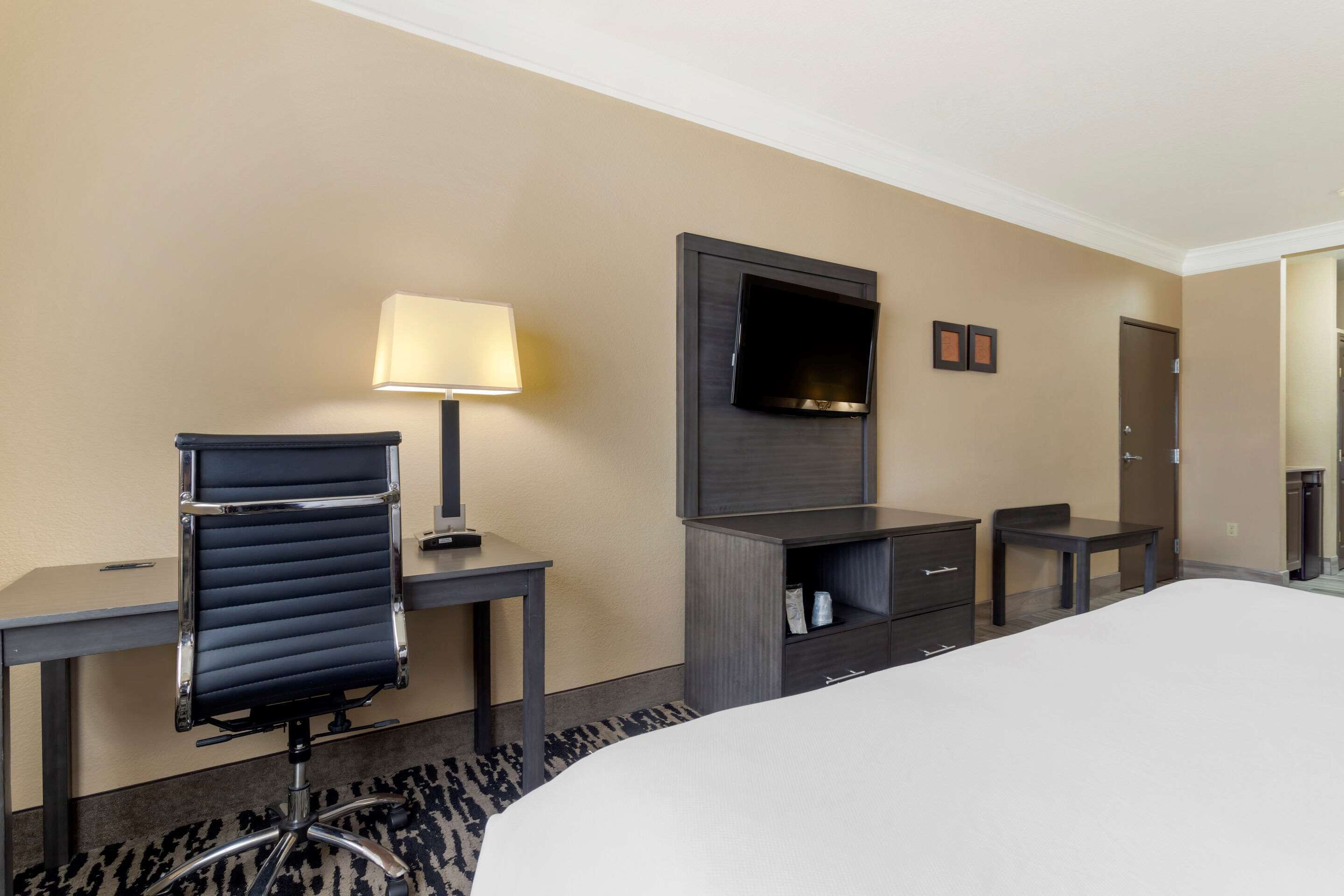 A hotel room with a bed, a desk with a chair, a TV mounted on the wall, a small table, and a wardrobe.