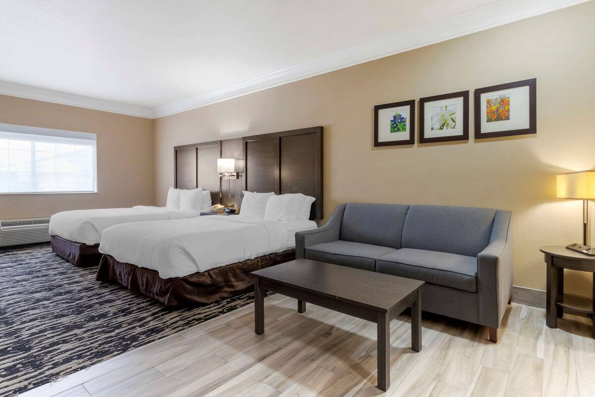 Een hotelkamer met twee bedden, een slaapbank, een salontafel en drie afbeeldingen in lijsten aan de muur.