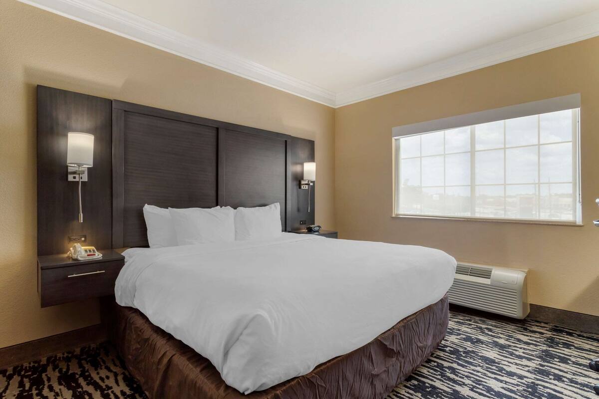 Een hotelkamer met een groot bed, een nachtkastje, een lamp, een raam en een airconditioning.