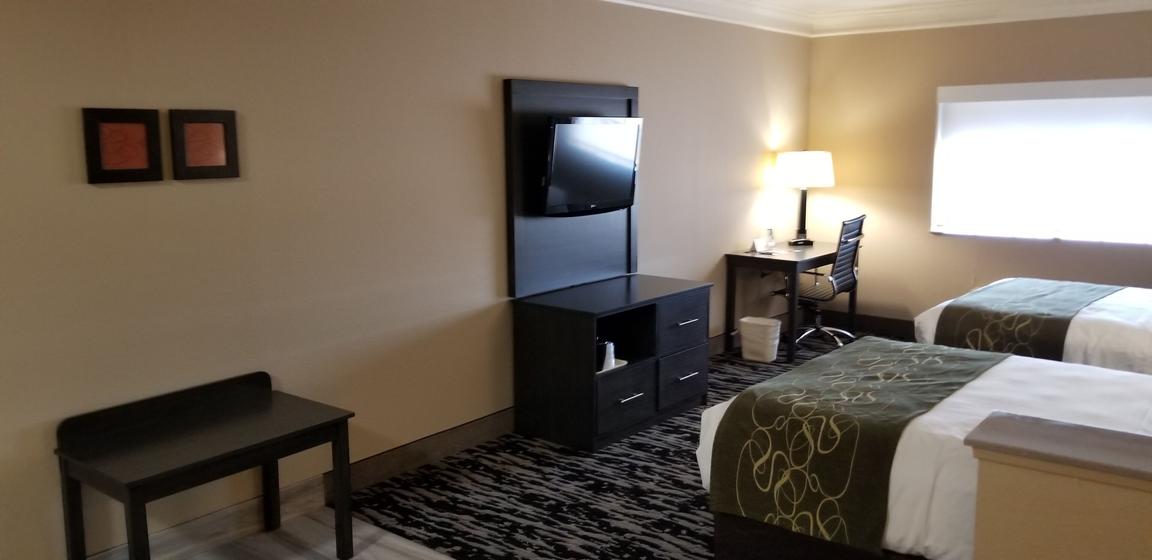 Ein Hotelzimmer mit zwei Betten, einem Schreibtisch mit Stuhl, einem Fernseher und einem kleinen Tisch.