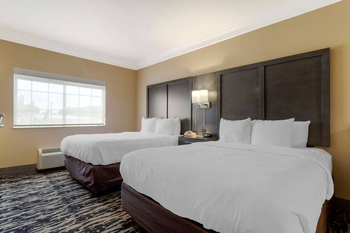 Een hotelkamer met twee bedden, een groot raam, een wandtafel en een wandlamp.