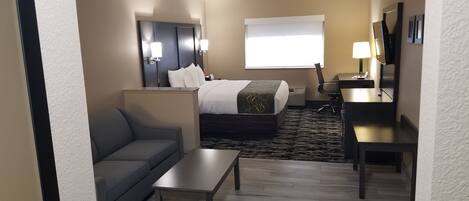Habitación de hotel con cama, sofá, escritorio, silla y televisión.