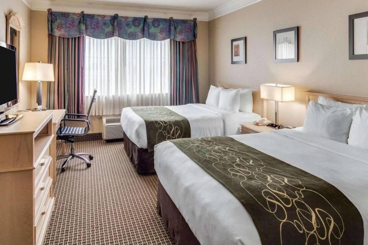 Een hotelkamer met twee bedden, een bureau met stoel, een televisie en een raam met gordijnen.
