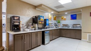 Zona de desayuno de hotel con cafetera, dispensador de zumo y enfriador para yogur.