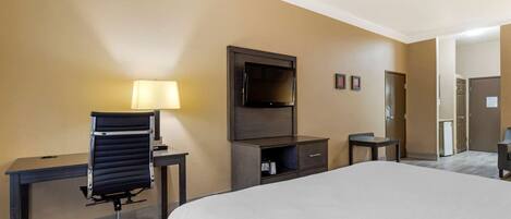 A hotel room with a bed, a desk, a chair, a TV, and a lamp.