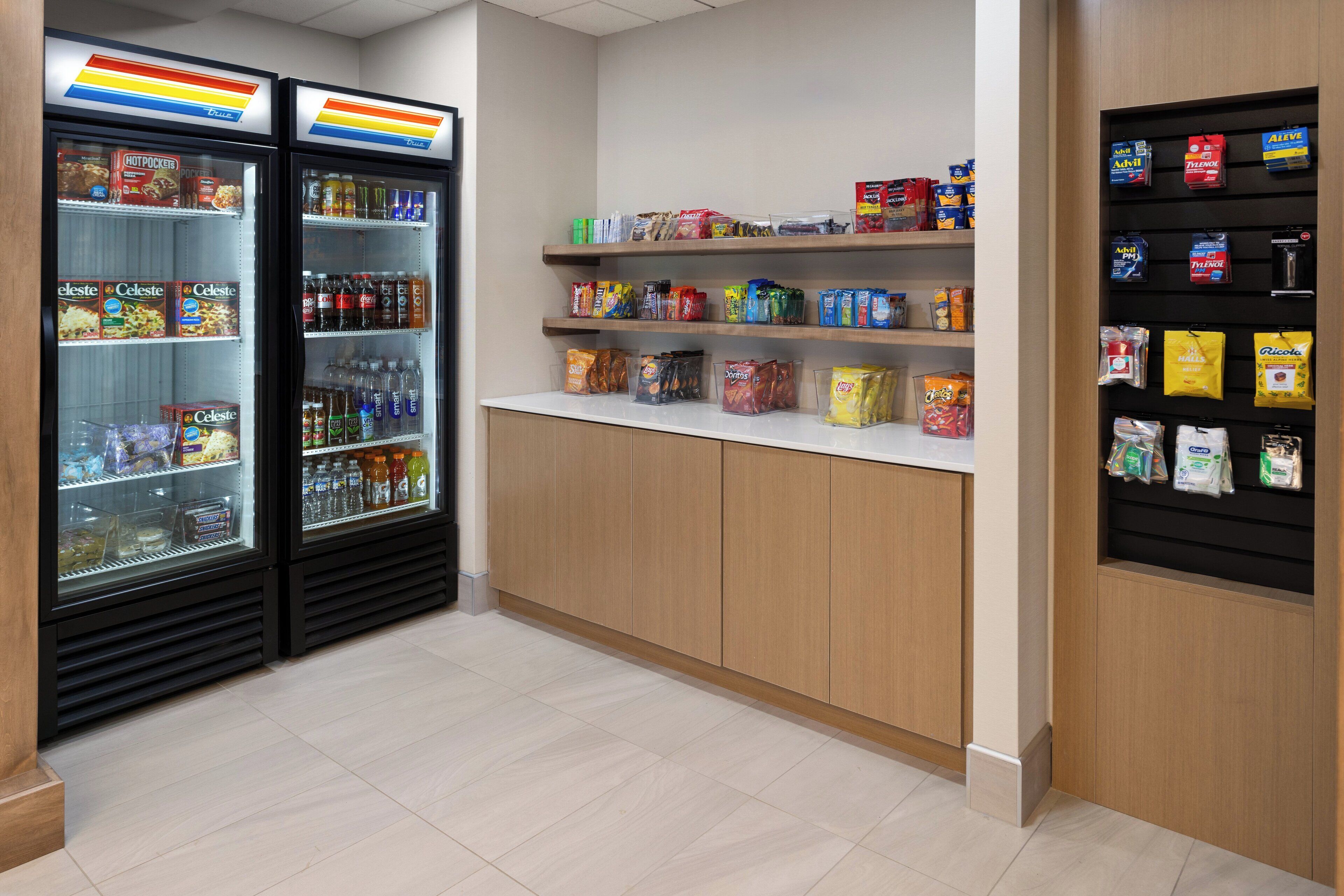 A clean, well-organized snack and beverage area with two refrigerated display cases, shelves stocked with snacks and drinks, and a counter with additional items.