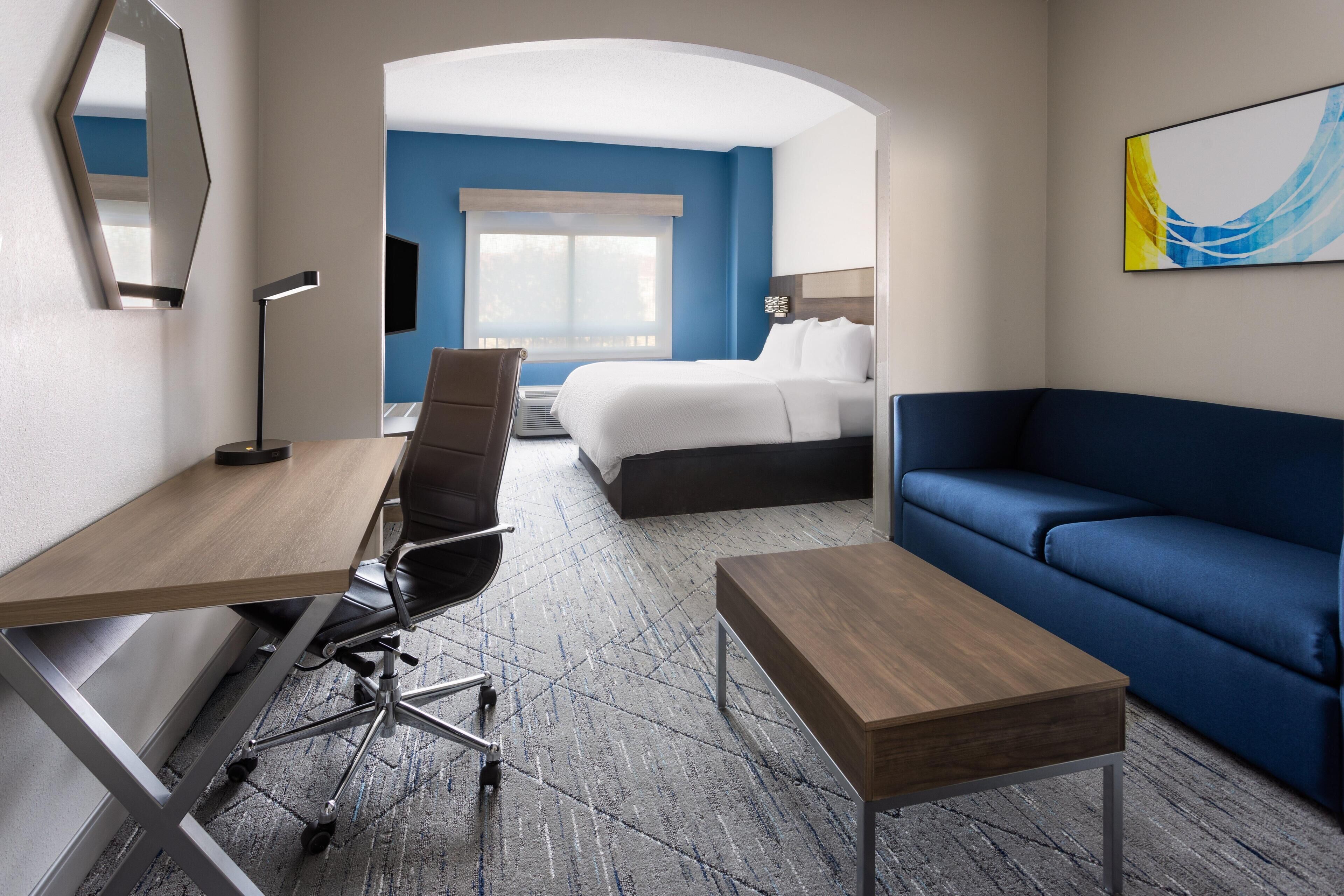 A hotel room with a desk, chair, sofa, bed, and a large window.