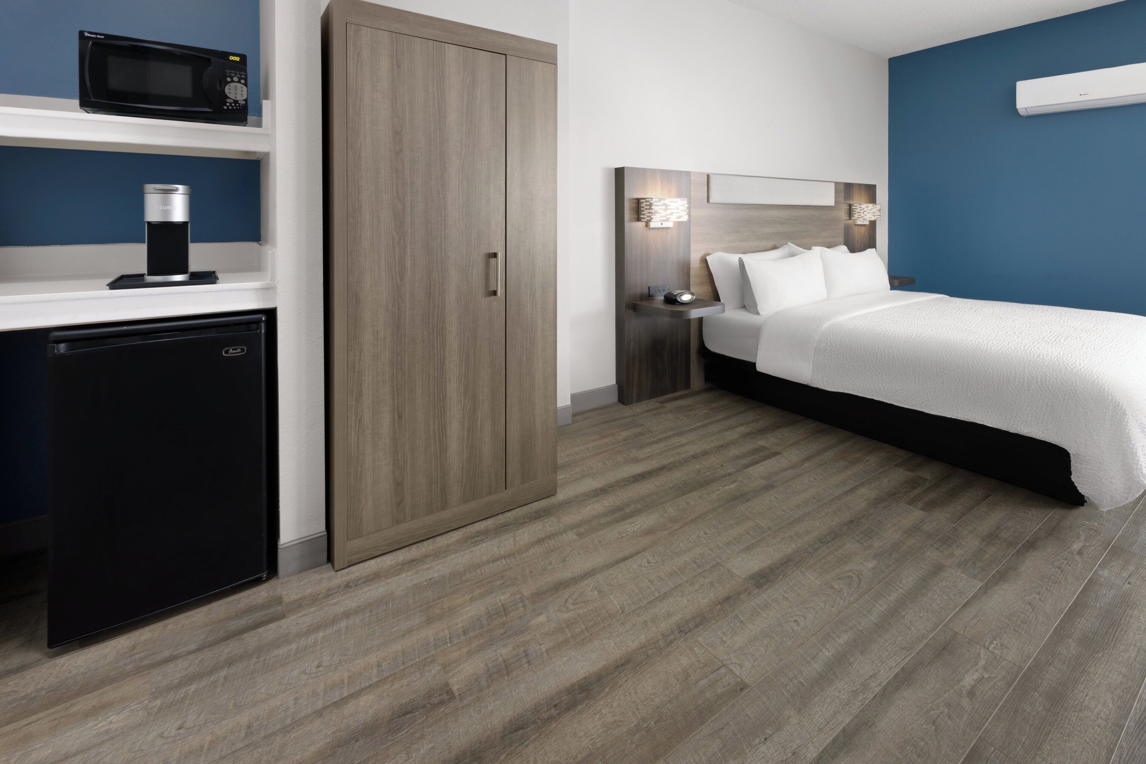 Habitación de hotel con cama, armario, mini refrigerador, microondas y estante con cafetera.