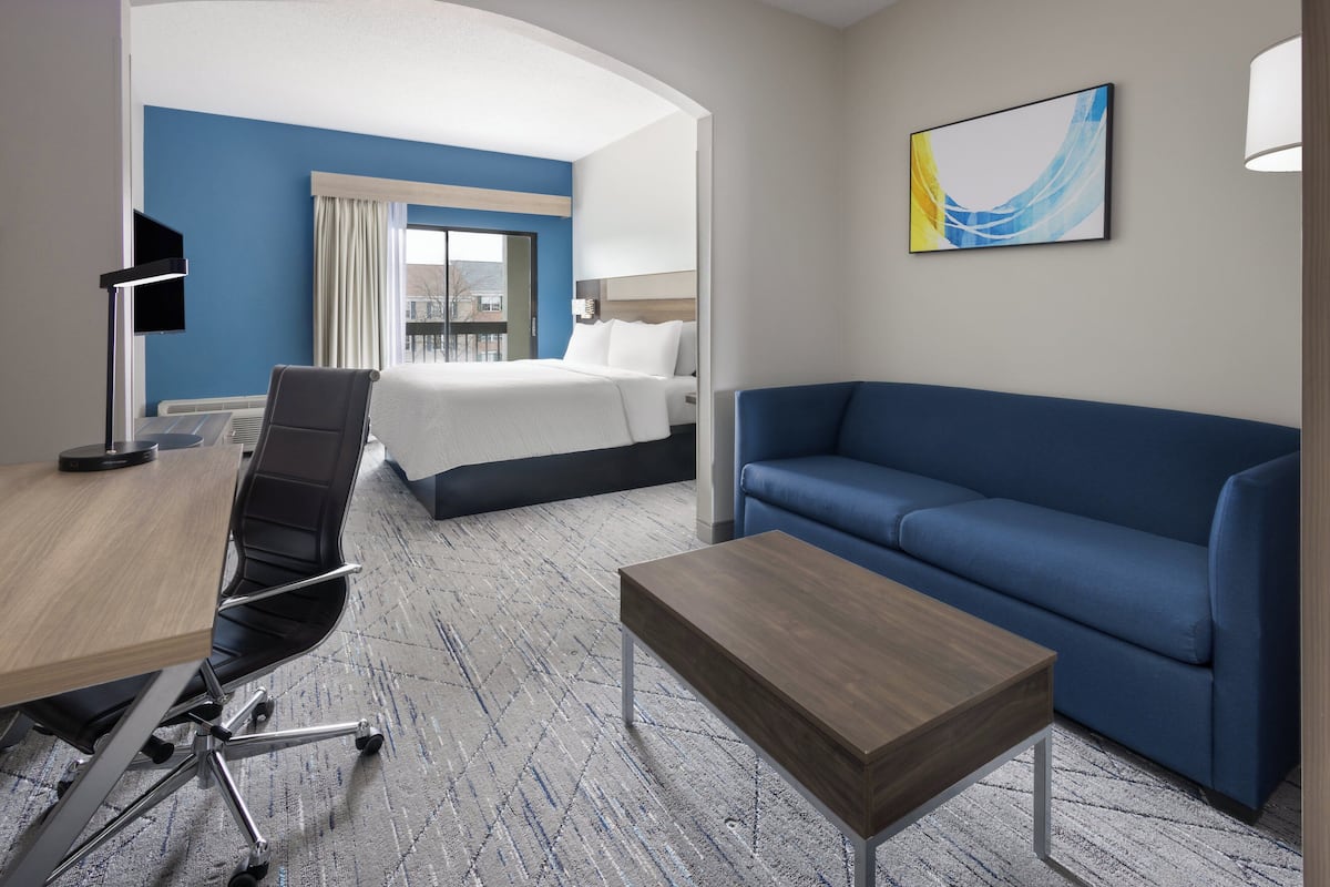 A hotel room with a bed, a blue sofa, a desk with a chair, and a lamp.
