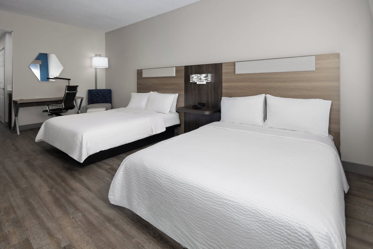 A hotel room with two beds, a desk, a chair, a lamp, and a mirror.