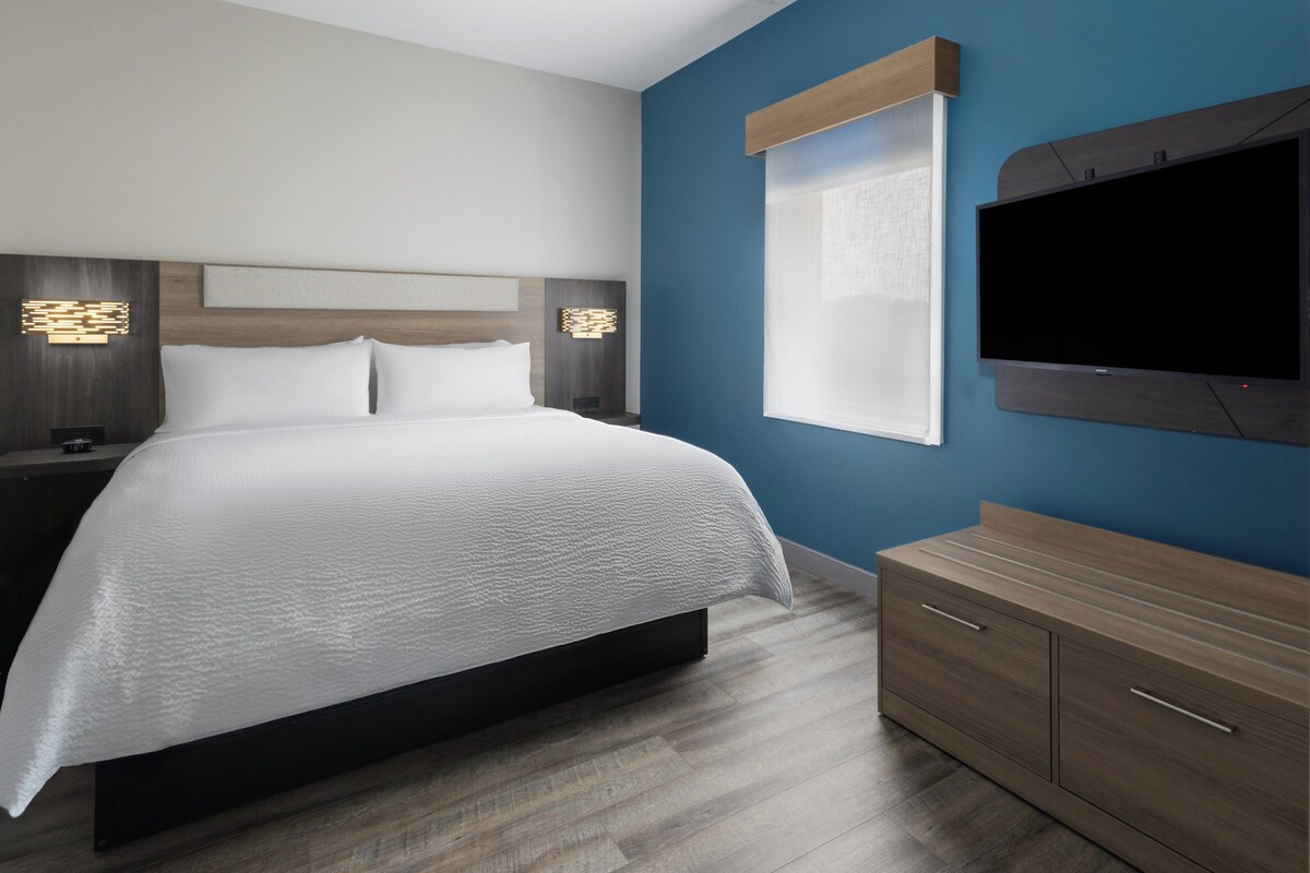 A modern hotel room with a large bed, a TV mounted on the wall, and a wooden dresser.