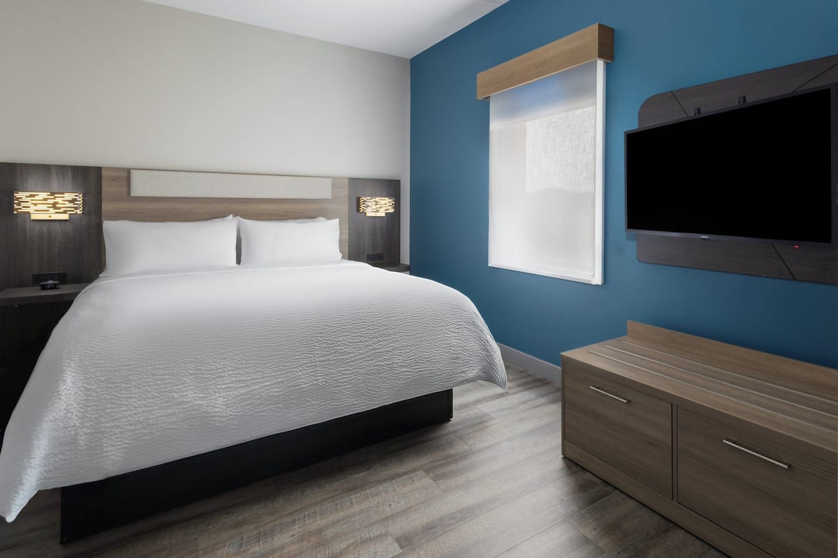 A modern hotel room with a large bed, a TV mounted on the wall, and a wooden dresser.