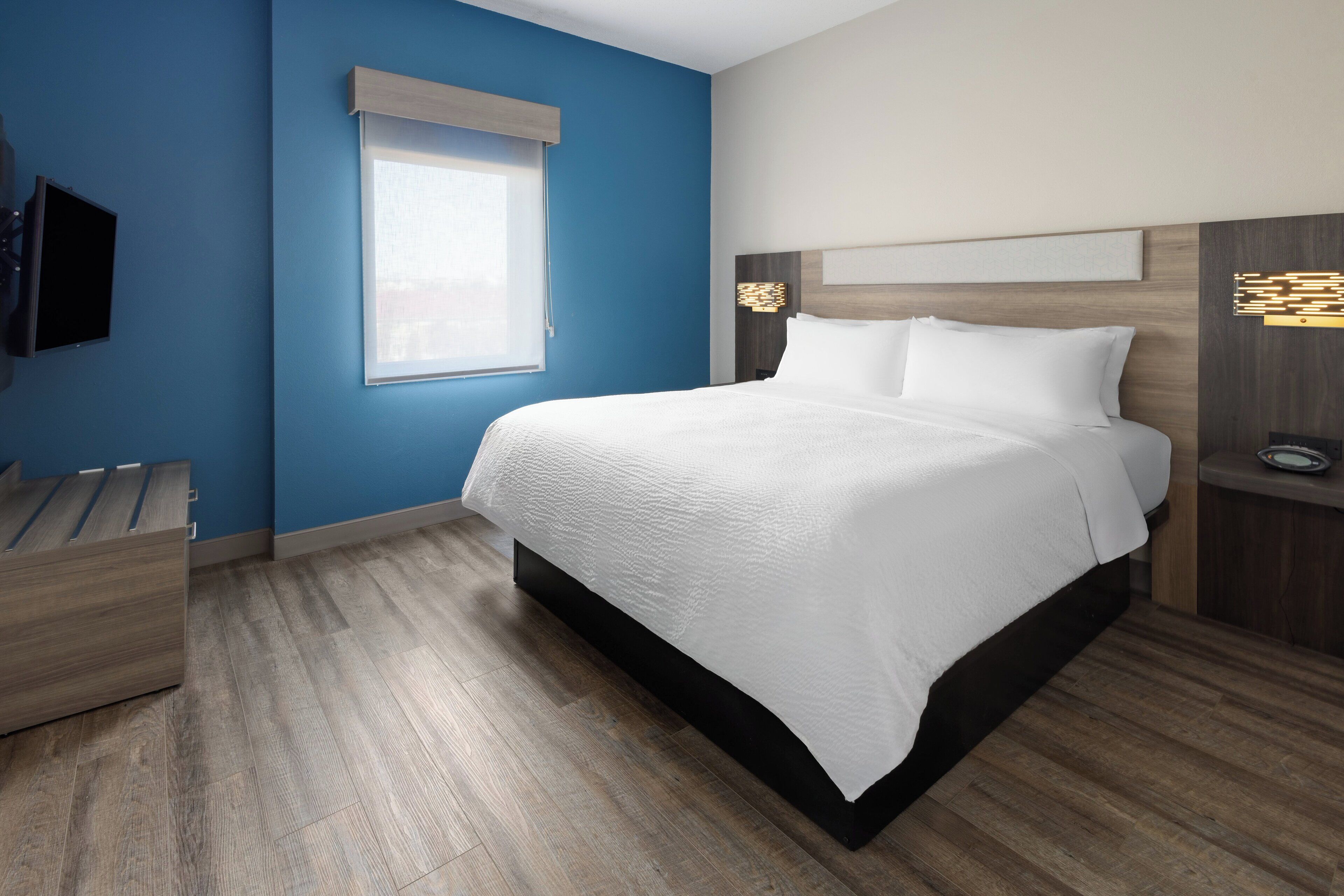 Una habitación de hotel moderna con una cama grande, un televisor y una mesita de noche de madera.