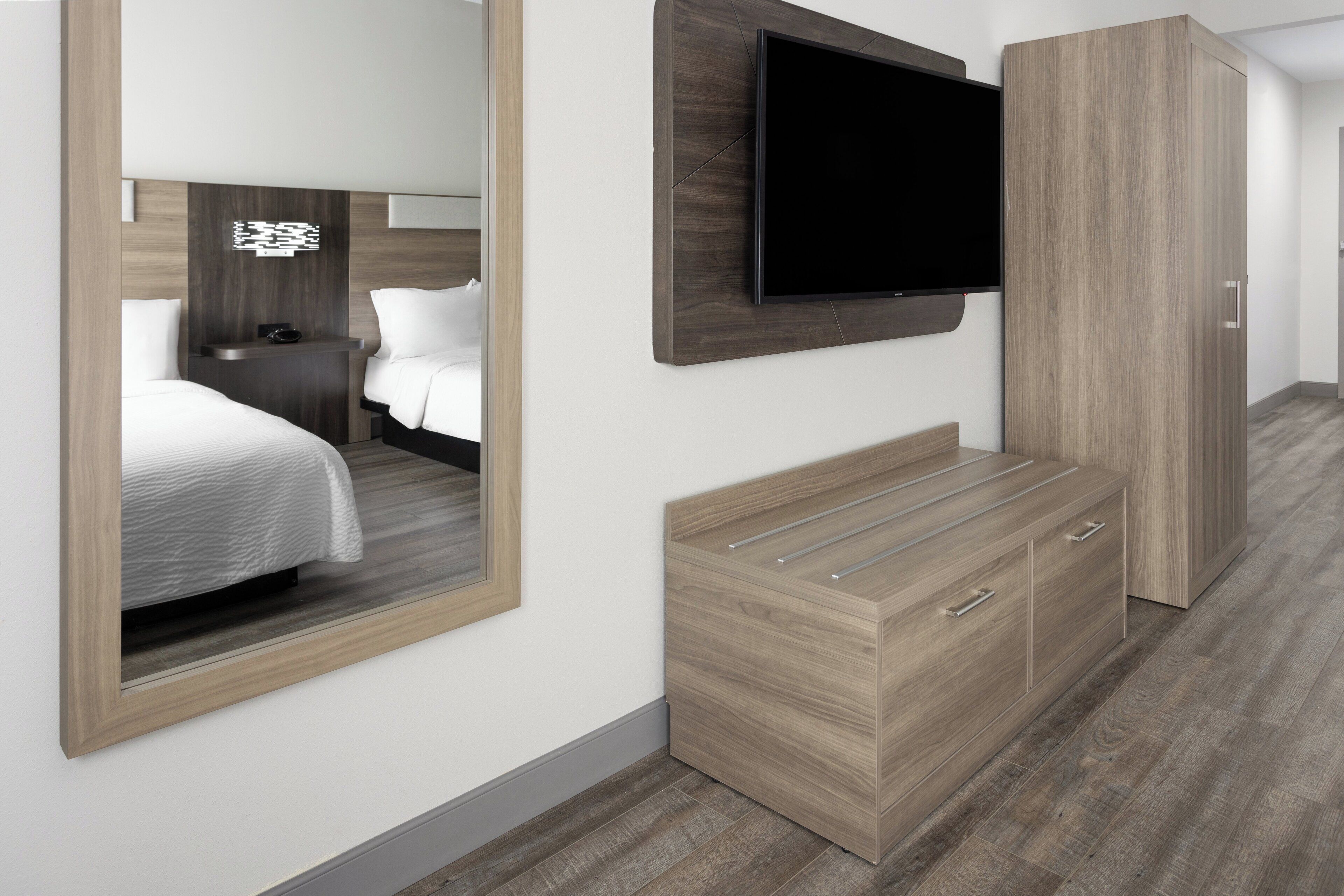 A hotel room with a bed, a TV mounted on the wall, a wardrobe, and a mirror.