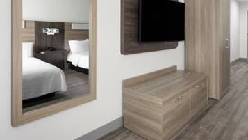 A hotel room with a bed, a TV mounted on the wall, a wardrobe, and a mirror.