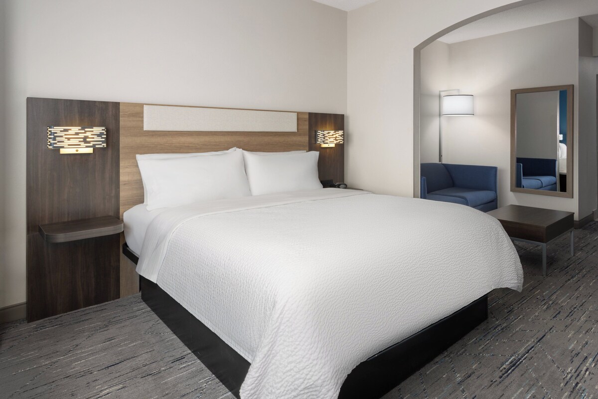 A modern hotel room with a large bed, a nightstand, a desk, a chair, and a mirror.