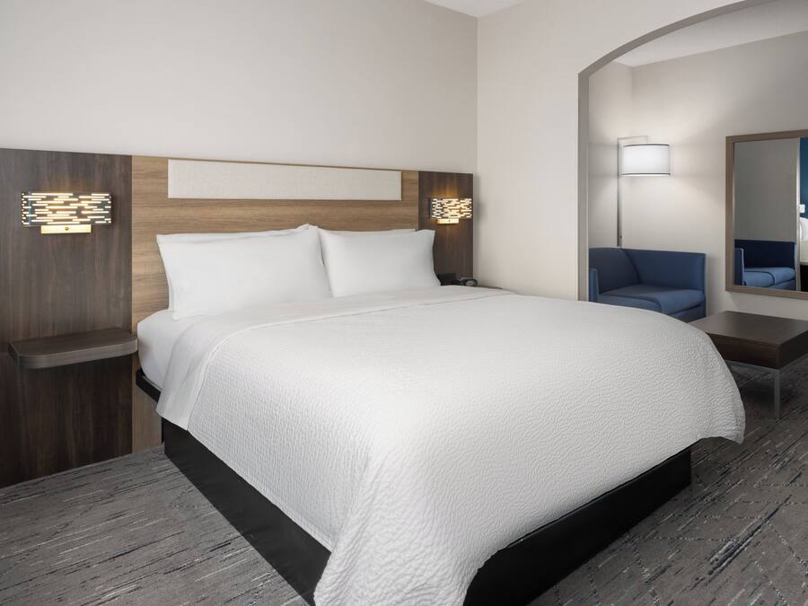 Una habitación de hotel moderna con una cama grande, una mesita de noche, un escritorio, una silla y un espejo.
