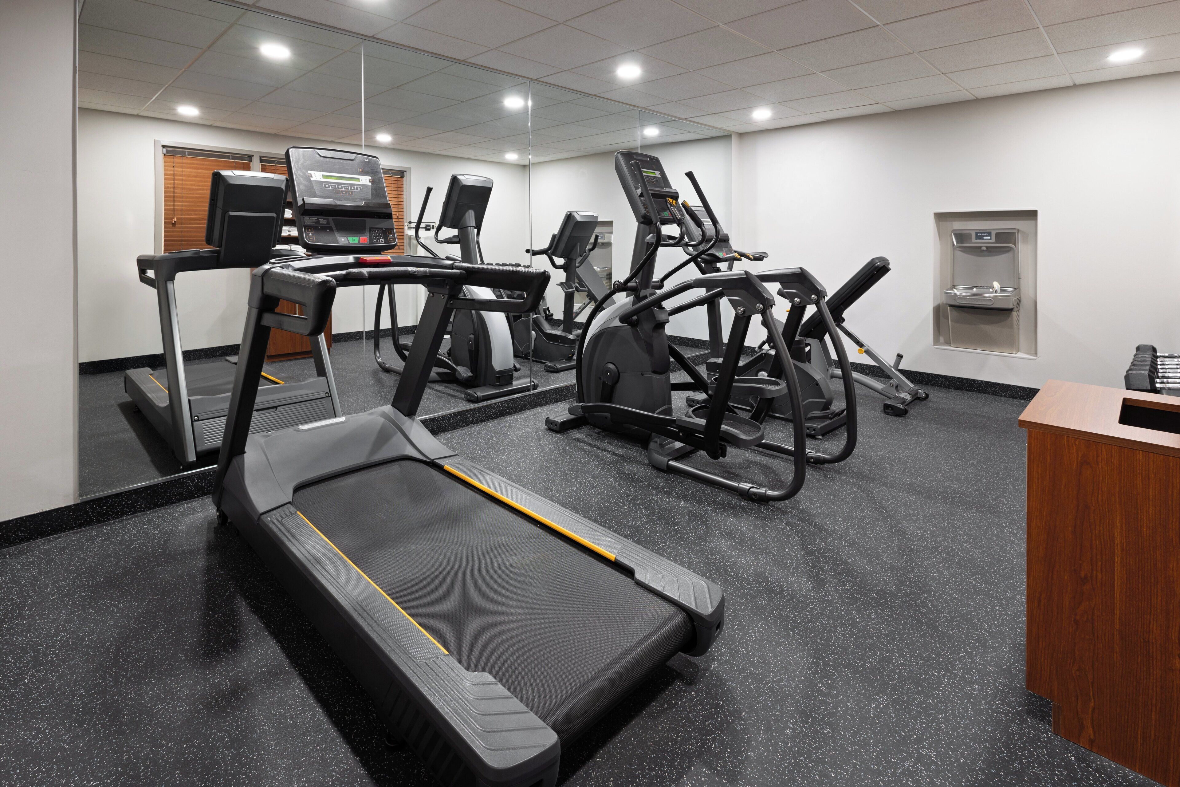 Une salle de sport équipée de tapis de course, de vélos elliptiques et d’un distributeur d’eau.