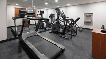 Une salle de sport équipée de tapis de course, de vélos elliptiques et d’un distributeur d’eau.