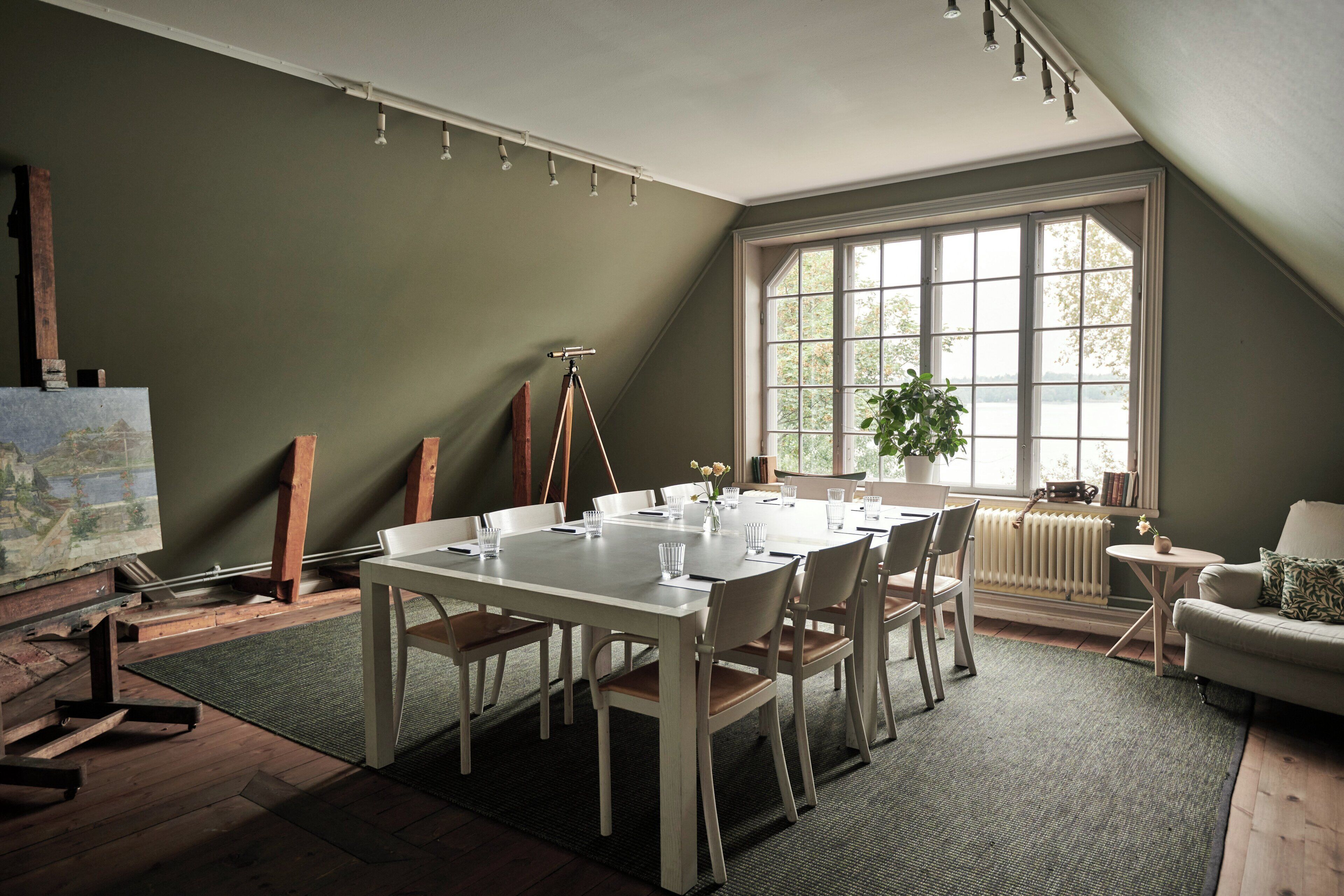 A dining area with a table set for six, a tripod, and a painting on the wall.