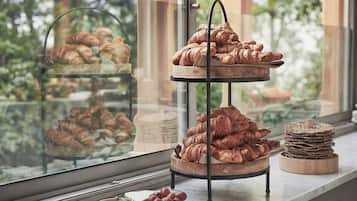 Mostrador de panadería con croissants y una pila de galletas junto a una ventana que da a zonas verdes.