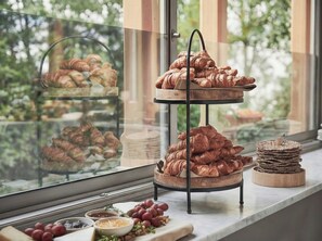 A bakery display with croissants and a stack of cookies by a window with a view of greenery. - Hotel J, Stockholm, a Member of Design Hotels (Nacka)