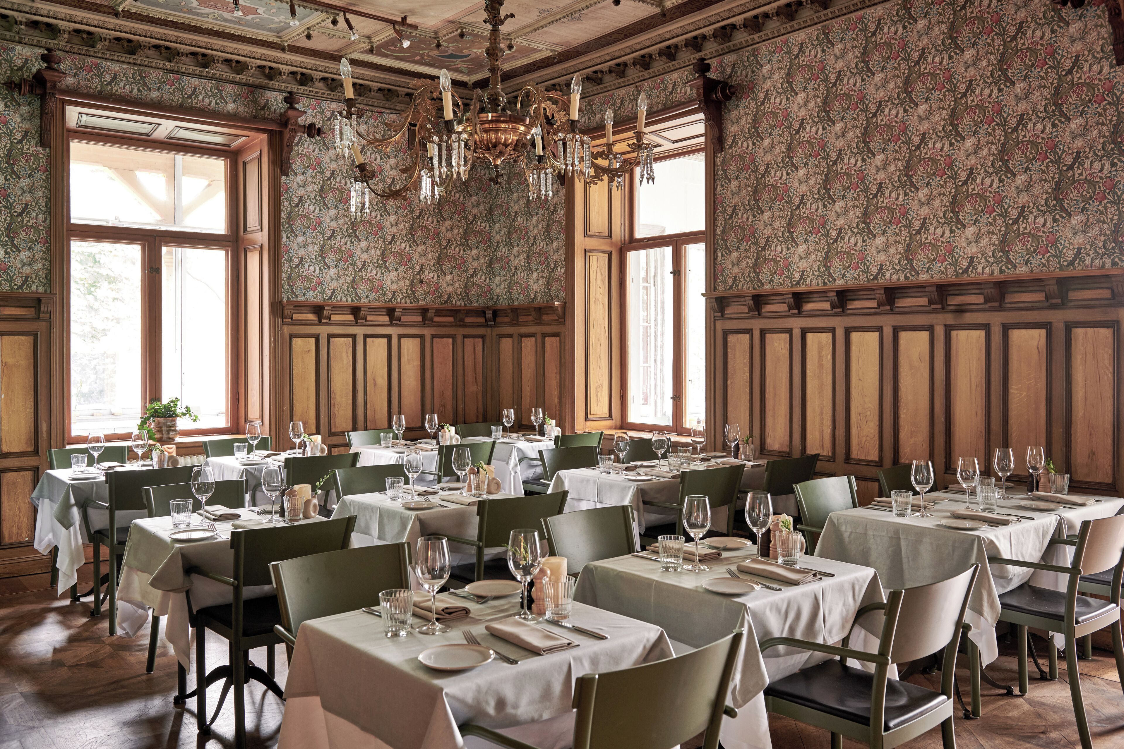 A dining area with multiple tables set for service, wooden paneled walls, and a chandelier.