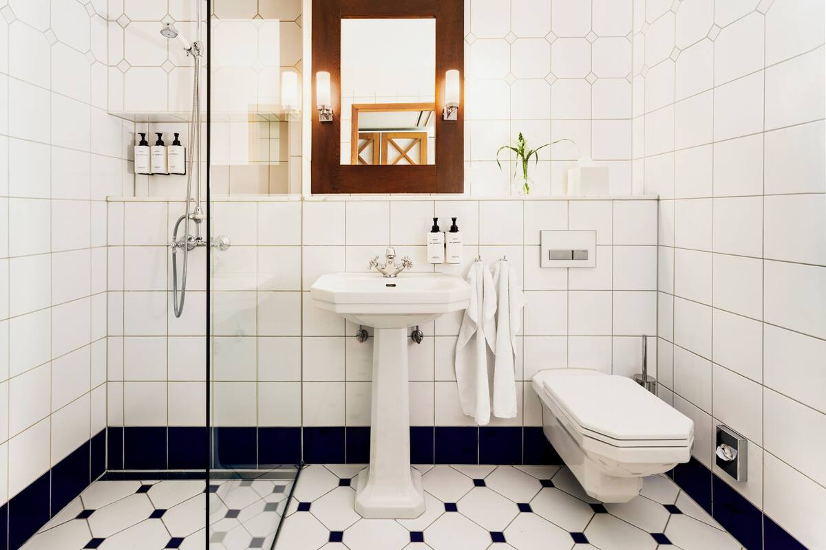 Une salle de bain avec un lavabo blanc, des toilettes et une douche. On y trouve des articles de toilette accrochés au mur et un miroir au-dessus du lavabo.