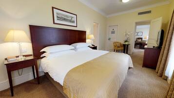 A hotel room with a large bed, two bedside lamps, a framed picture on the wall, a small table with a lamp, and a chair.