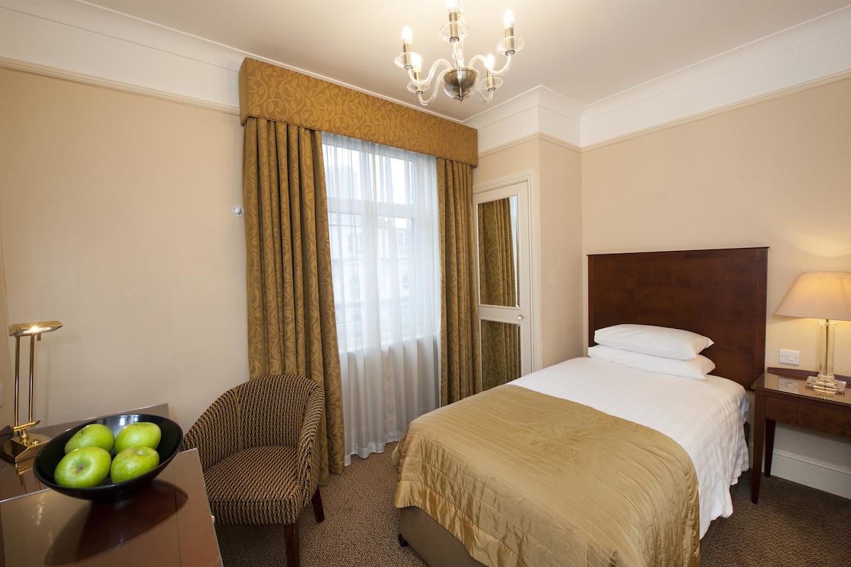 Une chambre d’hôtel avec un lit, une chaise, un bureau avec une lampe et un bol de pommes.